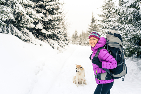 Happy girl hiking in white winter forest with akita dog. Recreation fitness and healthy lifestyle outdoors in nature. Inspirational winter landscape.の写真素材