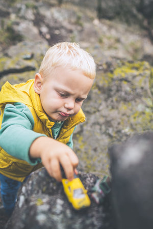 Toddler boy playing with toys on a rock. Little child walking on rocky mountains.