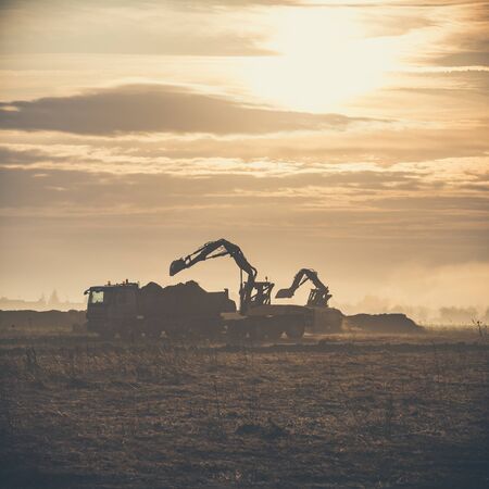 Excavator working on construction site, loading a dump track at sunrise.の写真素材