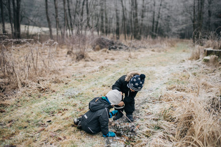 two little boys in dark clothes and a cap with stars playing with ice in frozen threshing