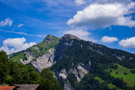 Swiss mountain landscape green grass, blue sky, white clouds, summer day, peakの写真素材