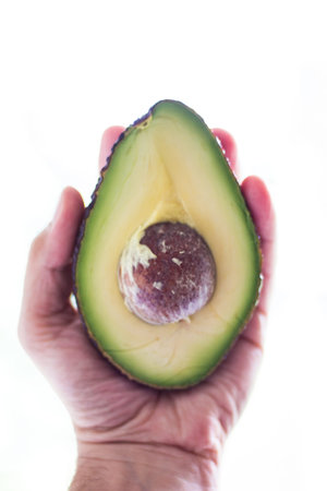 Half of freshly cut avocado with seed in male palm close up isolated against white background 2019