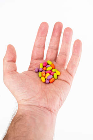Caucasian male extended opened hand with colored small cylindrical candy resting in his palm isolated against bright white background 2020の写真素材