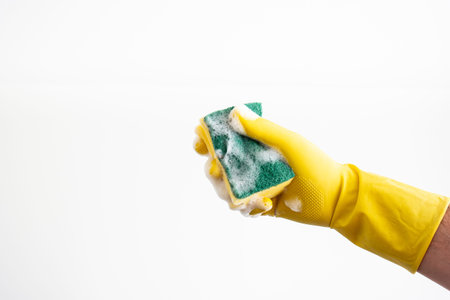 White Caucasian male hand with yellow latex glove holding a wet and soapy cleaning sponge against...