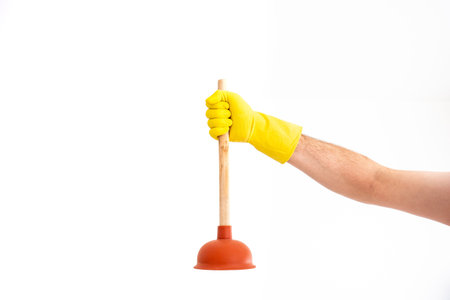 White Caucasian male hand with yellow latex glove holding a sink plunger against white background...