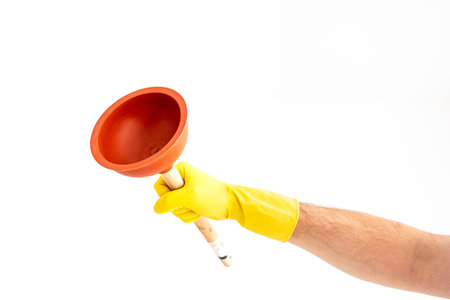 White Caucasian male hand with yellow latex glove holding a sink plunger against white background...