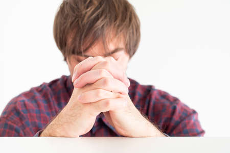 White Caucasian male in burgundy red shirt praying with his hand together closed eyes isolated against white background 2020の写真素材
