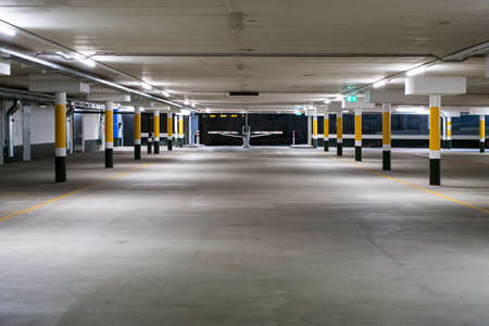 Inside underground large empty parking lot with barrier entrance at night illuminated by neon light 2020の写真素材