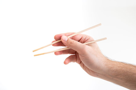 Asian chop sticks held by Caucasian male hand close up shot isolated on white 2020