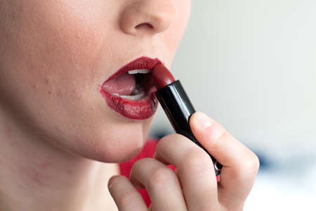 Caucasian while young female applying red crayon make up on her lips close up shot unrecognizable 2020の写真素材