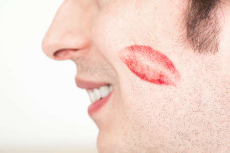 Caucasian white male man cheeks with red lipstick kiss marks smiling no face isolated against white 2020の写真素材