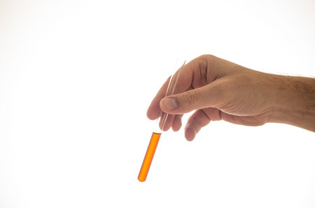 Glass cylindrical vial with orange brown liquid held by Caucasian male hand close up isolated on...