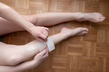 Caucasian young woman waxing her legs at home on the apartment floor no face unrecognizable 2020の写真素材