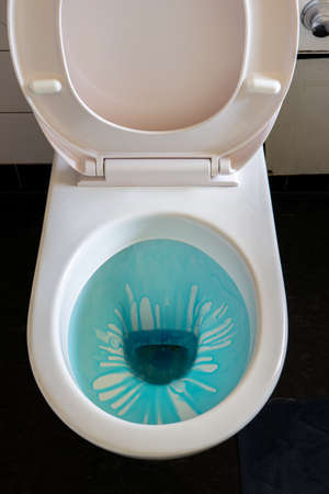 Clean toilet bowl with blue cleaning liquid gel ad the seat up in a small bathroom 2020の写真素材