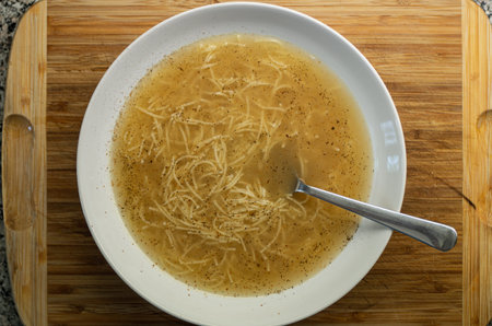 Cooked Veal soup with egg noodles in a white bowl and metal spoon set on wood board in the kithen 2020の写真素材