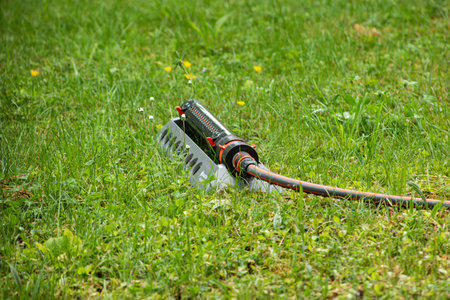 Large garden lawn water sprinkler system with hose set on a green grassy field no operating summer...