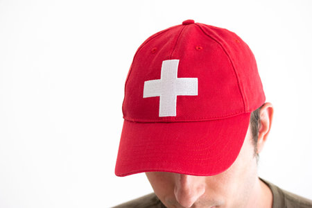 Adult Caucasian male head shot wearing red baseball hat with Swiss national symbol close 2020