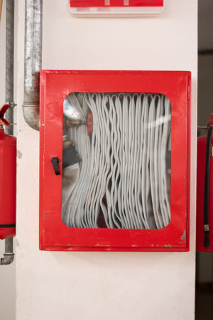Fire hose mounted on factory wall in closed emergency break red box.