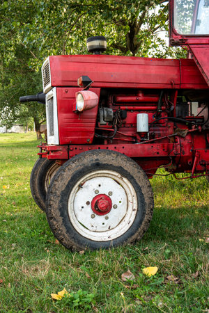 Old small red agriculture tractor parked on the grass summertime before sunset three-quarter view.