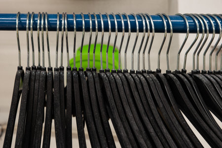 Row of black plastic coat hangers hanging on a metal pole inside factory ready for use.