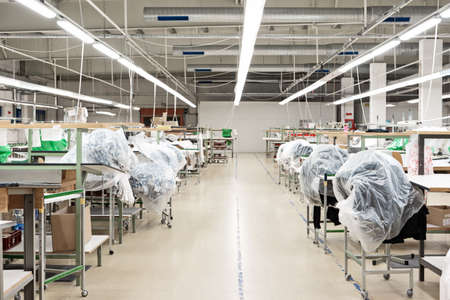 Small out of business garment factory production lines with groups of industrial sewing machines covered up in foil and carton.の写真素材