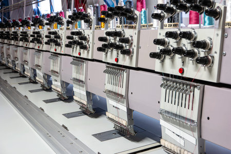 Multi head industrial sewing machine close up view inside small out of business factory warehouse.