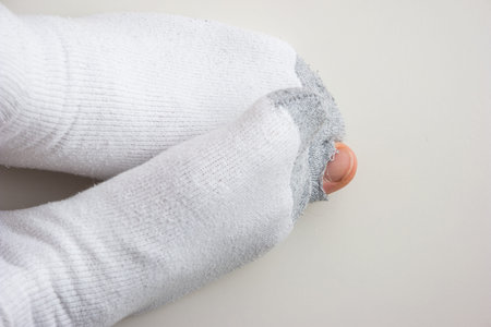Caucasian male toe sticking out of worn out short white socks with hole top view.