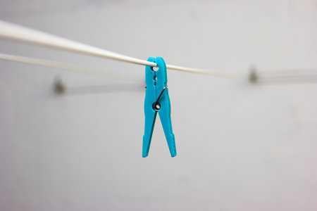 Light blue plastic laundry clip on a hanging wire indoor isolated shallow depth of field.