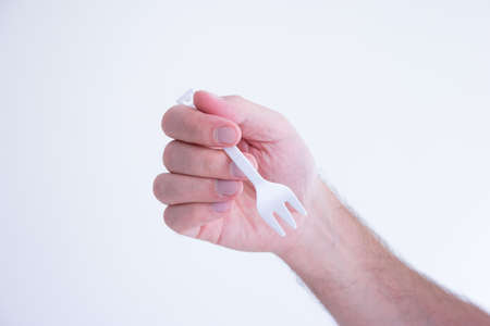 White plastic disposable fork modeled by Caucasian male hand isolated on white.の写真素材