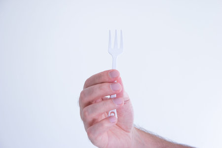 White plastic disposable fork modeled by Caucasian male hand isolated on white.