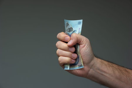 Caucasian male hand crushing a 100 Romanian lei bill close up shot isolated on gray.