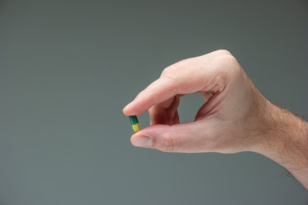 Caucasian male hand holding a yellow and green medicine capsule pill between fingers close up shot isolated studio shot.の写真素材