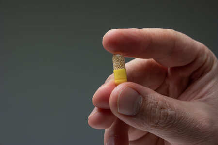 Caucasian male hand holding a yellow and white medicine capsule pill between fingers close up shot...