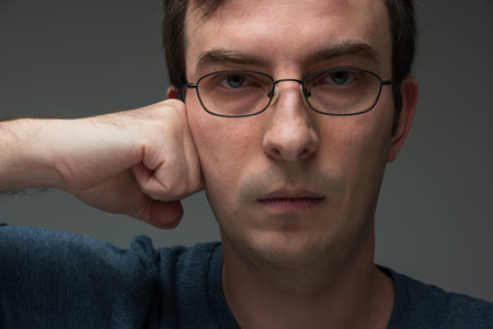 Caucasian male with glasses with clinched fist pressed against cheek looking at camera 30 to 40...