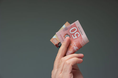 Caucasian male hand holding a folded 50 Canadian dollar bill close up shot isolated on gray.の写真素材