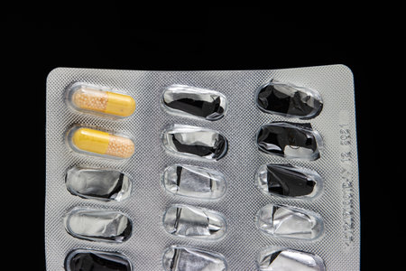 Yellow and white medical capsules in almost empty blister packs front view isolated on black.の写真素材