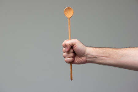 Caucasian male hand holding a wooden spoon close up shot isolated on gray background.の写真素材