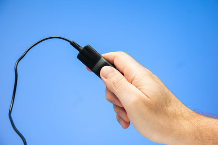Caucasian male hand holding and pressing a cable wired black plastic remote control unit isolated on...