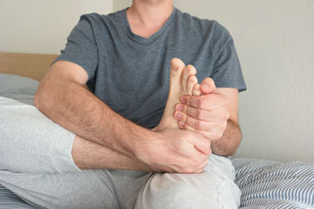 Caucasian male in pain holding his bare right foot with two hands unrecognizable no faceの写真素材