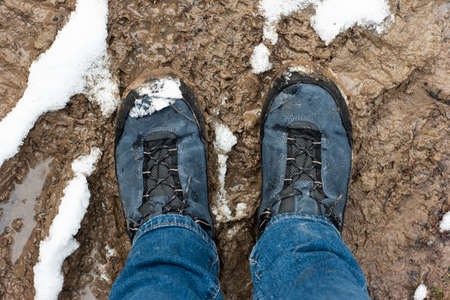 Dirty weatherproof boots in a forest mud puddle with melting snow blue jeans top view.の写真素材