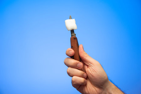 Single white marshmallow on a small pocket knife blade held in hand by Caucasian male hand isolated...