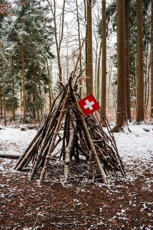 Tree branch made wooden tent play hut in the forest flying a small Swiss national flag.