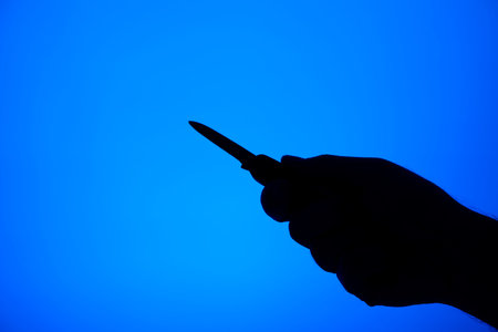 Knife stabbing gesture silhouette black on blue background studio shot unrecognizable .