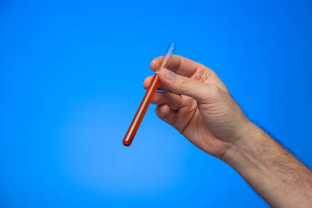 Test tube vial with red liquid held by Caucasian male hand isolated on blue background studio shot.の写真素材