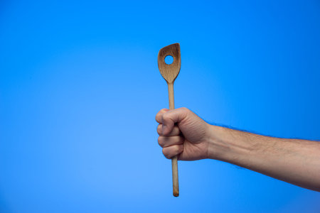 Caucasian male hand holding a wooden spoon close up shot isolated on blue background.