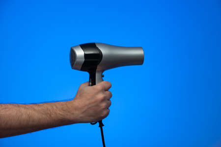 Caucasian male extended arm holding a hair dryer isolated on blue background studio shot.の写真素材