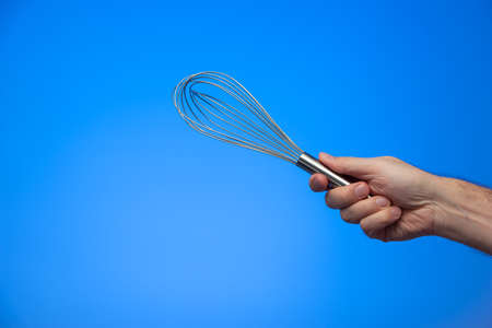 Caucasian male hand holding silver metal whisker isolated on blue background.の写真素材
