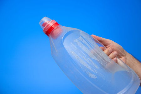 Caucasian male hand holding a large empty plastic bottle with dew and droplets upside down isolated...