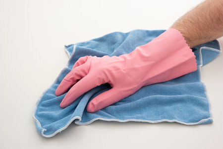 Pink latex cleaning glove on Caucasian male hand holding a blue microfiber cloth making cleaning...