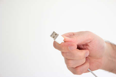 USB cable ad connector held in hand by Caucasian male hand isolated on white background.の写真素材